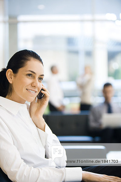 Young businesswoman sitting in lobby  using cell phone  smiling