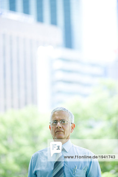 Mature businessman outdoors  frowning at camera  head and shoulders