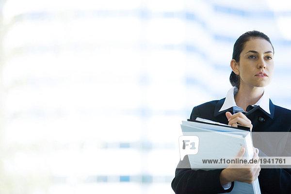 Young businesswoman holding binder  looking away  waist up
