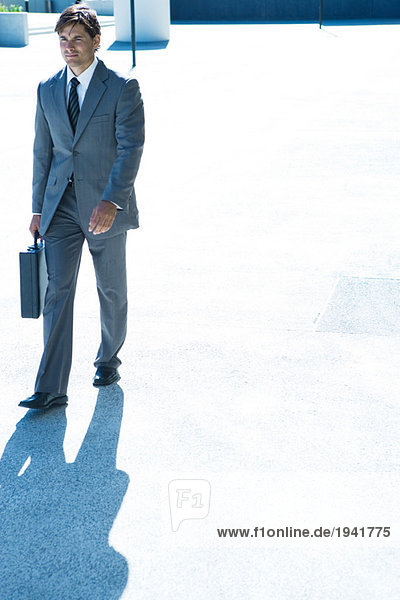 Young businessman walking outdoors  carrying briefcase  full length