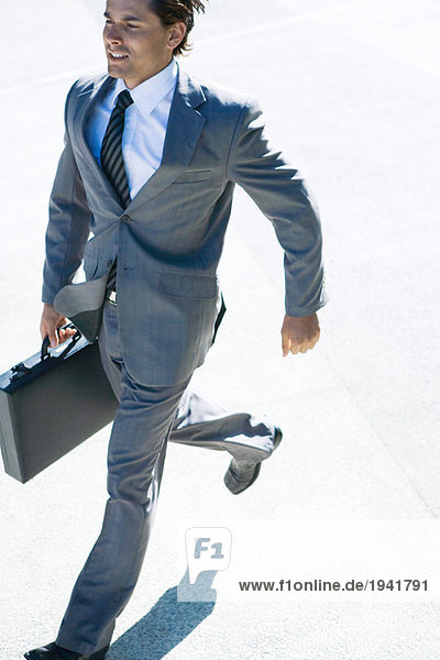 Ein junger Geschäftsmann  der im Freien läuft und eine Aktentasche trägt.