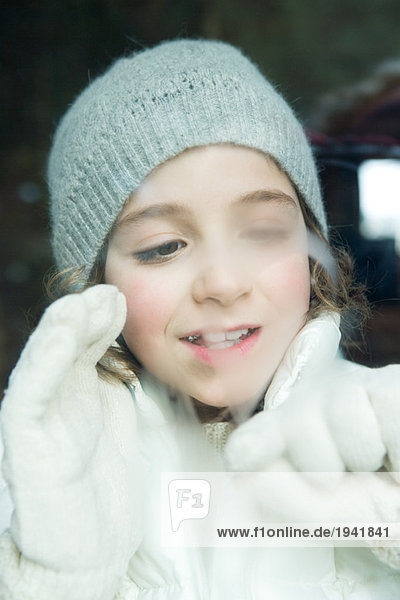 Girl breathing on window  drawing with glove  dressed in winter clothing