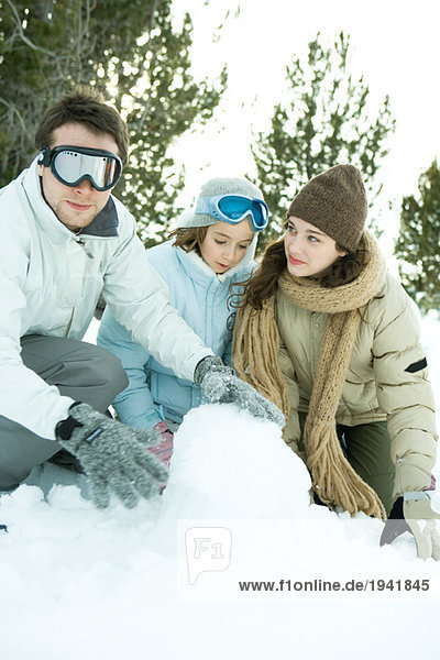 Three young friends crouching in snow  making snowball  one looking at camera
