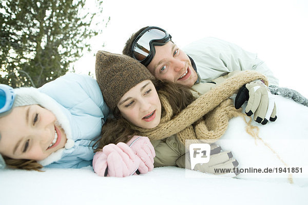 Three young friends reclining in snow  piled up  one smiling at camera
