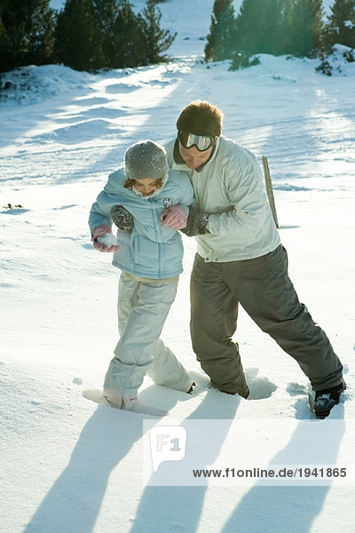 Junger Mann  der der kleinen Schwester hilft  im Schnee zu laufen  beide mit Blick nach unten  volle Länge.