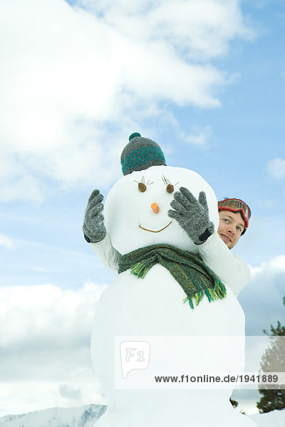 Young man embracing snowman  looking around  portrait