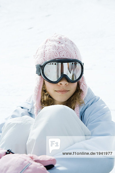 Preteen girl wearing ski gear  sitting in snow  hugging knees  portrait