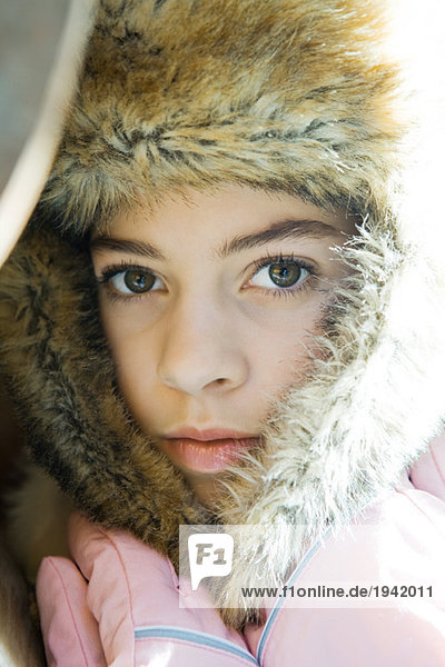 Preteen girl  wearing fur hat  holding flaps together over neck  close-up portrait