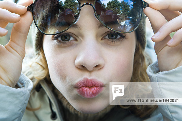 Preteen girl lifting sunglasses  puckering at camera  close-up