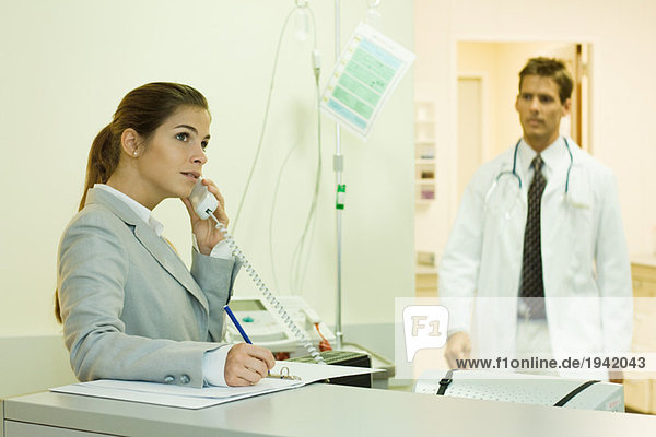 Frau telefoniert in der Arztpraxis  Ärztin nähert sich im Hintergrund