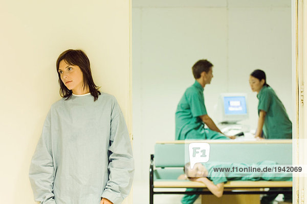 Patientin steht im Krankenhausflur  medizinisches Personal im Büro im Hintergrund