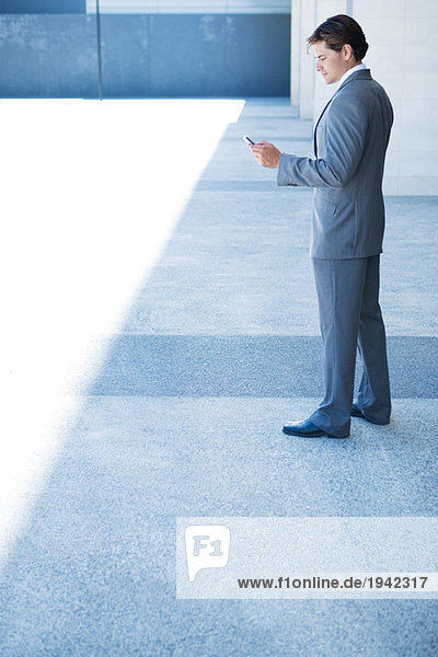 Businessman looking down at cell phone  full length