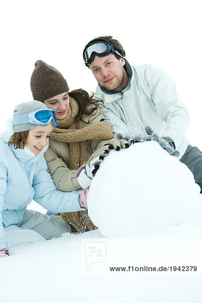 Three young friends making snowball  dressed in winter clothing  one looking at camera