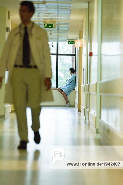 Mann sitzt  schaut aus dem Fenster  trägt Krankenhauskittel  Arzt geht in den Vordergrund