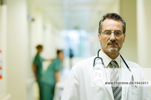 Male doctor standing in hospital corridor  looking at camera  head and shoulders