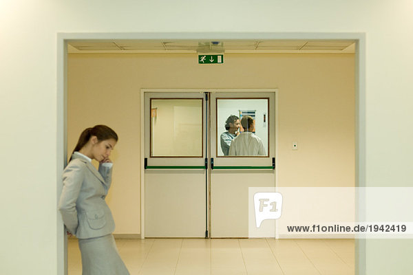 Frau mit Handy im Wartezimmer des Krankenhauses  Arzt und Patient im Hintergrund