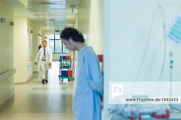 Male doctor walking in hospital corridor  patient in foreground