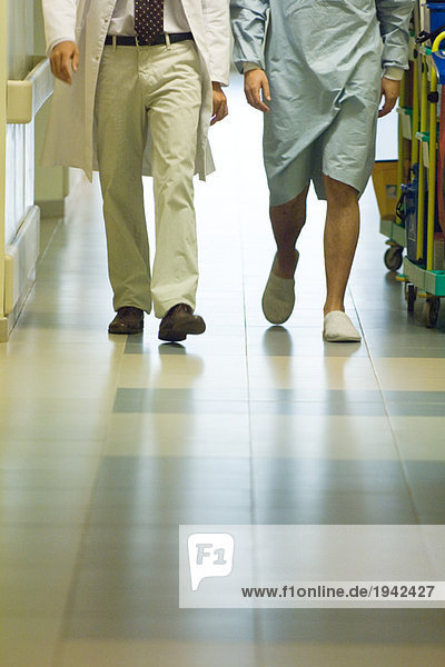 Männlicher Arzt beim Gehen mit Patient im Krankenhausflur  abgeschnittene Ansicht der Beine