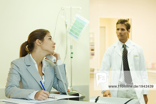 Woman using phone in doctor's office  looking over shoulder at male doctor