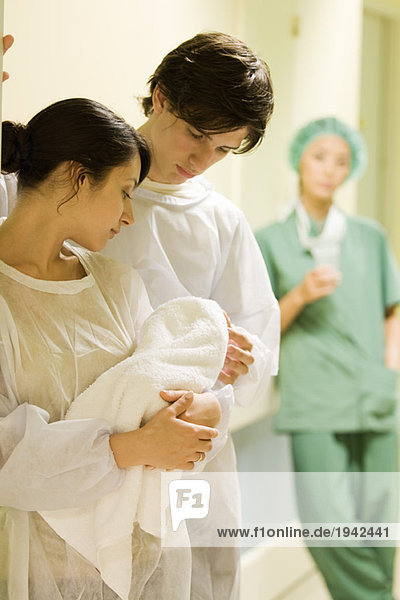 Paar stehend  gemeinsam auf das Neugeborene schauend  Arzt im Hintergrund