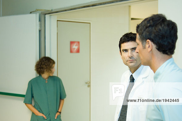 Mann stehend mit Arzt im Krankenhaus  Seitenansicht  Frau im Hintergrund