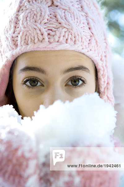 Preteen Mädchen hält eine Handvoll Schnee in Handschuhen und schaut in die Kamera.