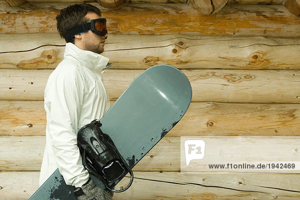 Junger Mann mit Snowboard  Seitenansicht