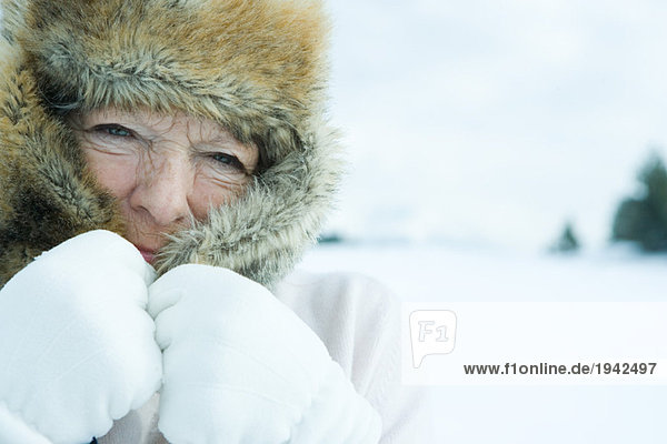 Seniorenfrau mit Fellmütze über dem Gesicht  in verschneiter Landschaft  Nahaufnahme