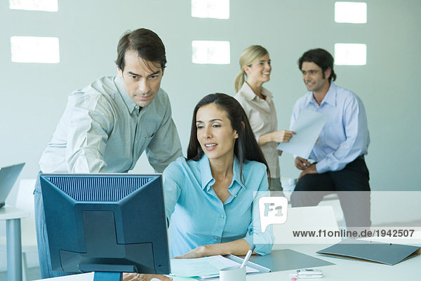 Businessman and businesswoman in office  looking at computer  associates in background