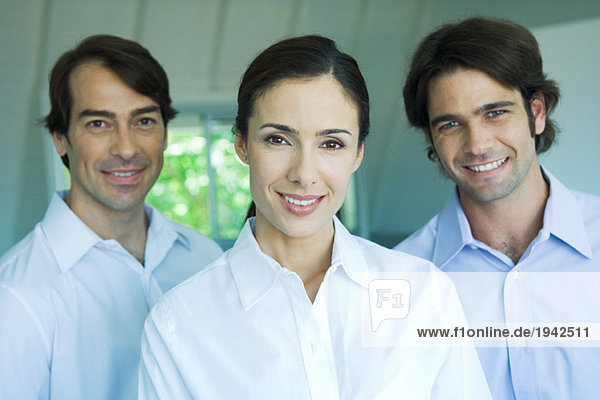 Businesswoman and two businessmen smiling at camera  head and shoulders  portrait