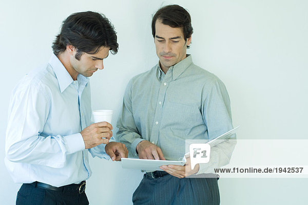 Two businessmen standing  looking at binder  waist up
