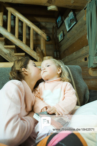Mädchen und Kleinkind sitzen auf der Couch  küssende Wange