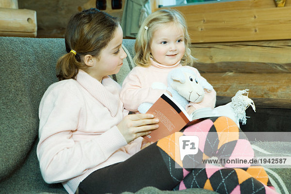 Mädchen und Kleinkind auf der Couch sitzend  lesend  lächelnd
