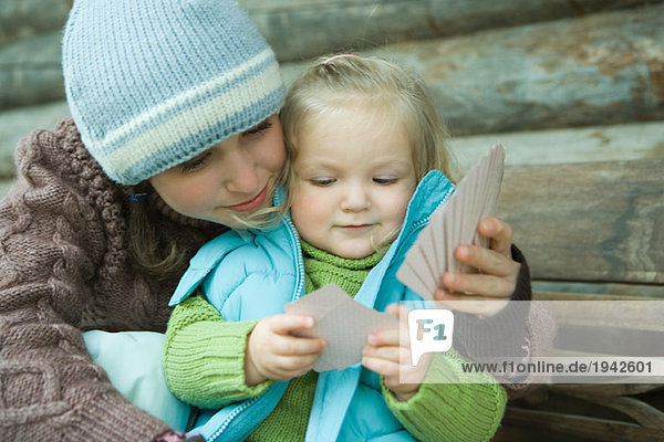 Teenager Mädchen und Kleinkind Spielkarten  gekleidet in Winterkleidung  Wange an Wange