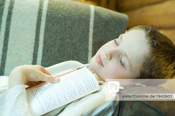 Junge auf Couch liegend  Buch haltend  Augen geschlossen