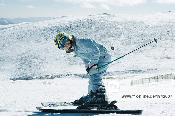 Junger Skifahrer beugt sich vor  lächelt in die Kamera  Ganzkörperporträt
