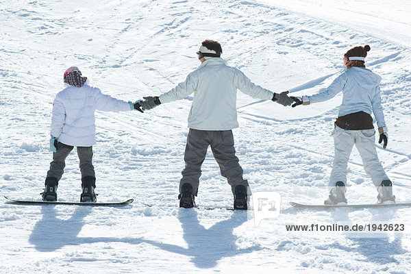 Drei junge Snowboarder stehen zusammen  halten Händchen  Rückansicht