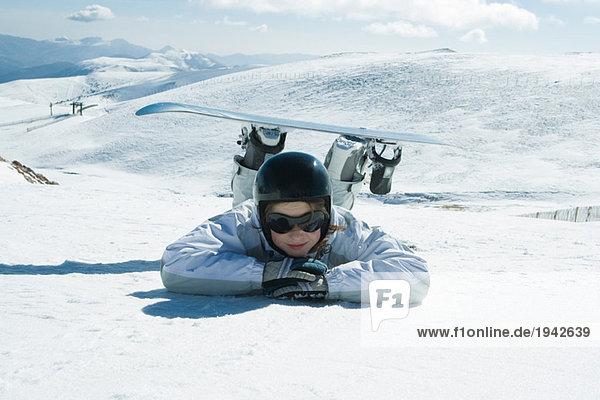 Young snowboarder lying on the ground  head resting on arms  smiling at camera
