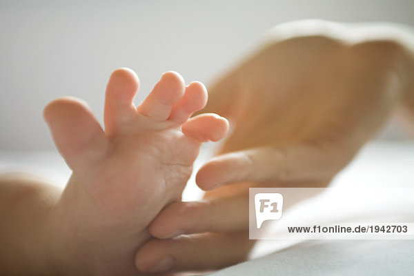 Ausschnitt einer erwachsenen Hand,  die den Fuß des Babys berührt,  Nahaufnahme