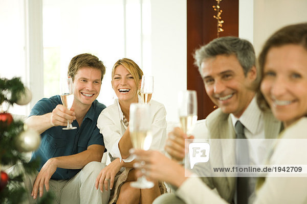 Erwachsene Freunde stoßen mit Champagner an und lächeln in die Kamera.