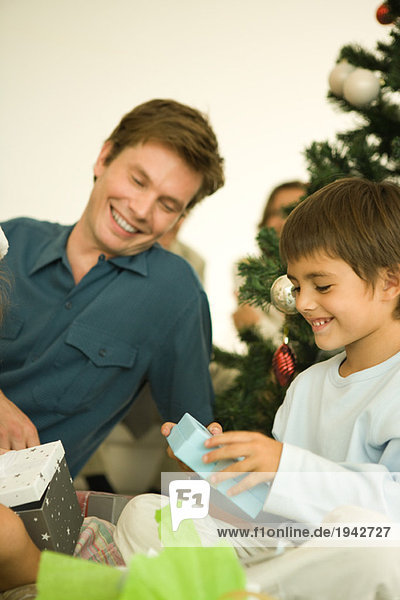 Mann und Junge am Weihnachtsbaum sitzend  Weihnachtsgeschenk zur Eröffnung  lächelnd