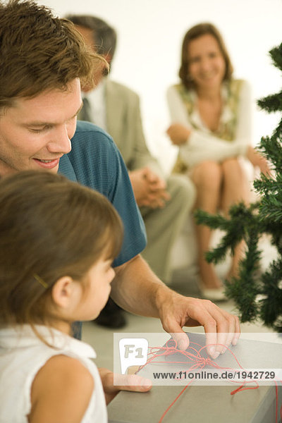 Mann und Mädchen eröffnen Weihnachtsgeschenk  Erwachsene im Hintergrund