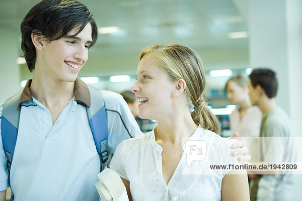Two students standing together  smiling at each other  one's arm around the other's shoulder
