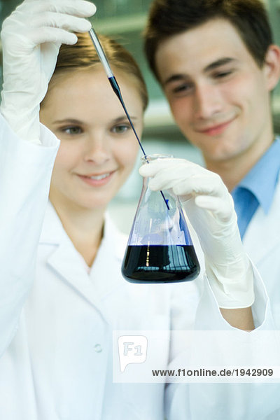 Junge männliche und weibliche Laboranten  die Laborglaswaren halten