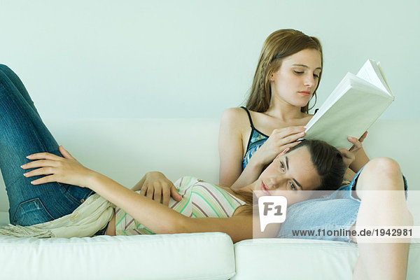 Junge Frau auf Couch Lesebuch  Freundin ruht Kopf auf dem Schoß
