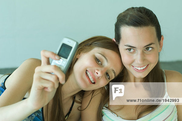Junge Frau fotografiert sich selbst mit Freundin  hält Handy hoch