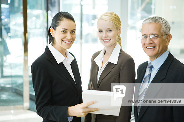 Geschäftspartner lächeln vor der Kamera  eine Frau hält einen Stapel Dokumente in der Hand.