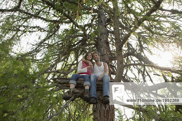 Junges Paar auf Baumhaus sitzend  umarmend