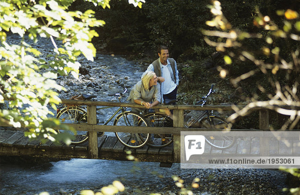 Paar mit Fahrrädern  auf Holzbrücke stehend  lächelnd