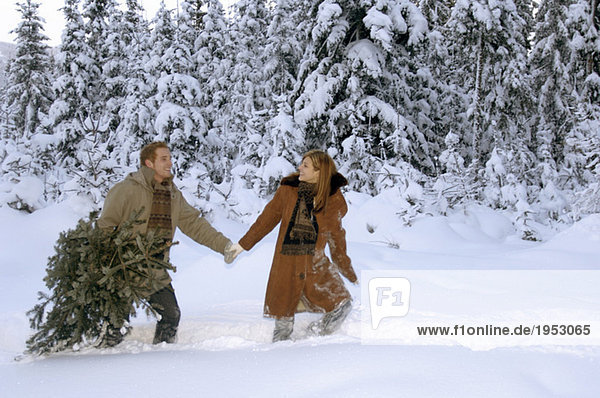 Junges Paar mit Weihnachtsbaum im Schnee